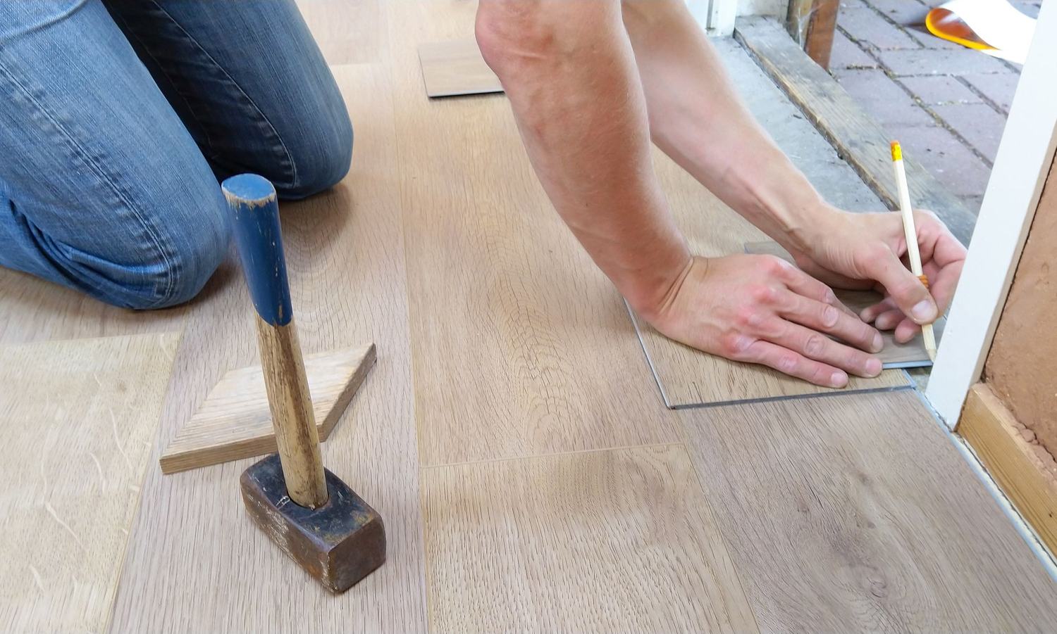 Ruky s kladivom pri kladení laminátovej podlahy